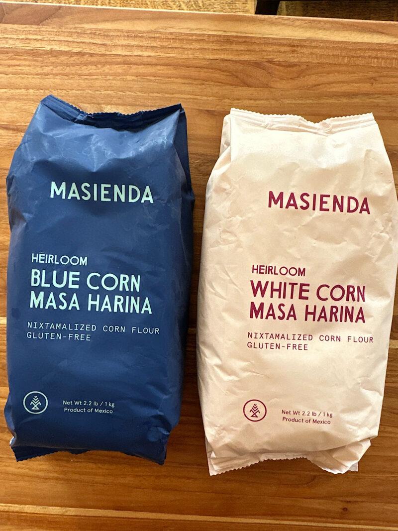 Two bags of heirloom masa harina, one blue corn and one white corn.