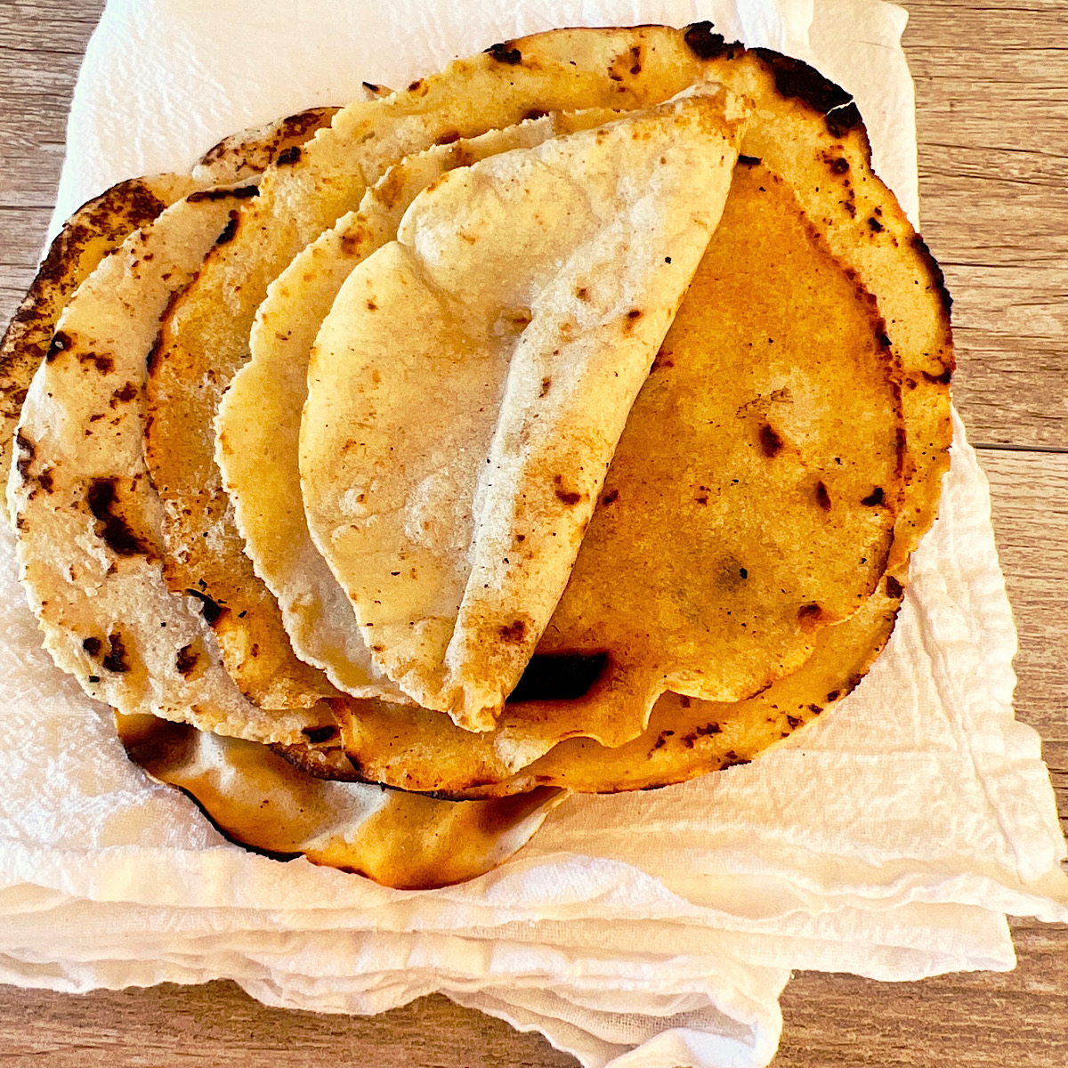 Stack of homemade corn tortillas on a white towel.