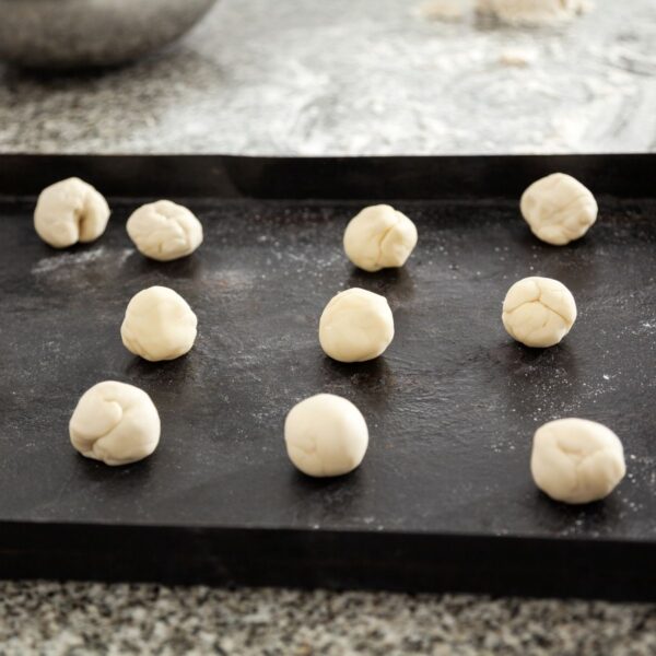 Small balls of masa dough laid out on black tray to rest before making tortillas.