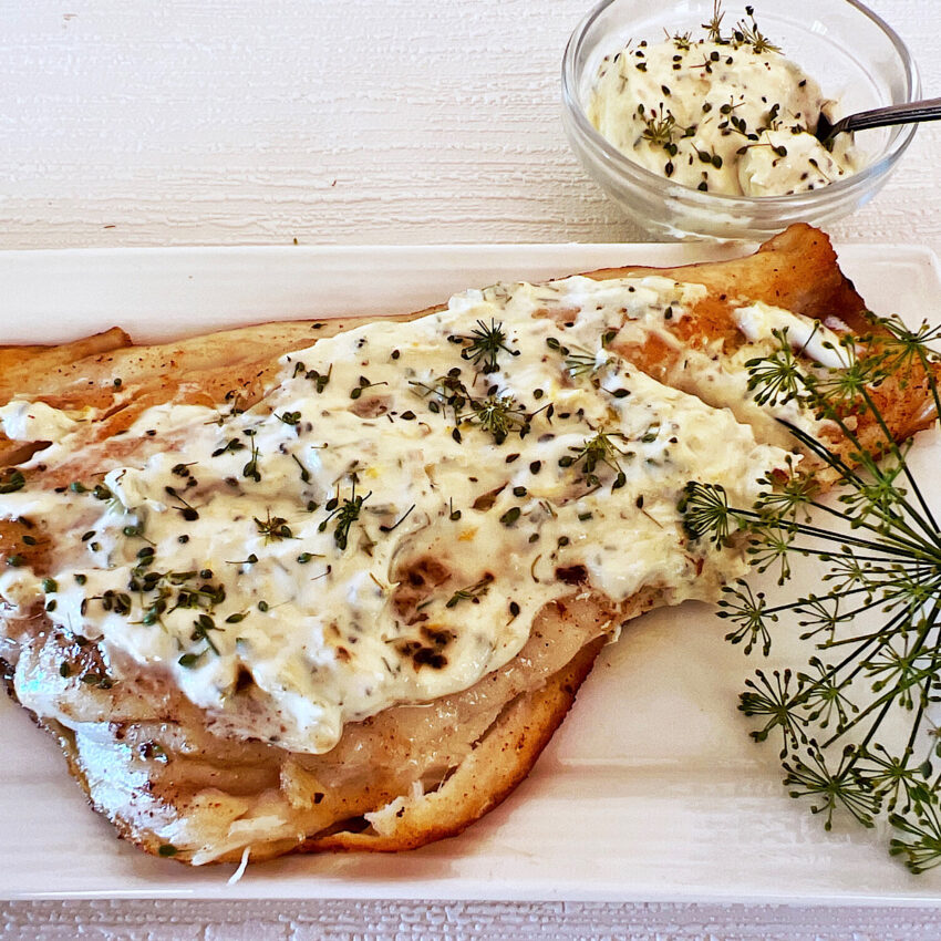 Fillet of red snapper covered with a sour cream dill sauce and a sprig of dill weed on the side.