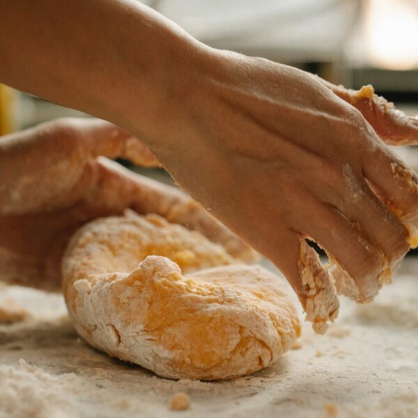 Hands kneading masa harina dough on a board covered with corn flour.