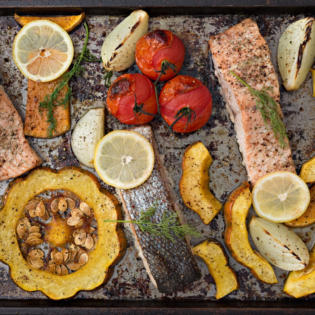 Fish and vegetables arranged on a sheet pan for roasting.