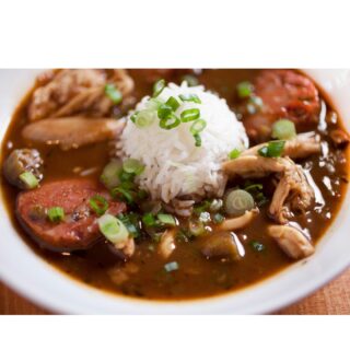 Cup of mounded rice in middle of bowl surrounded by gumbo.