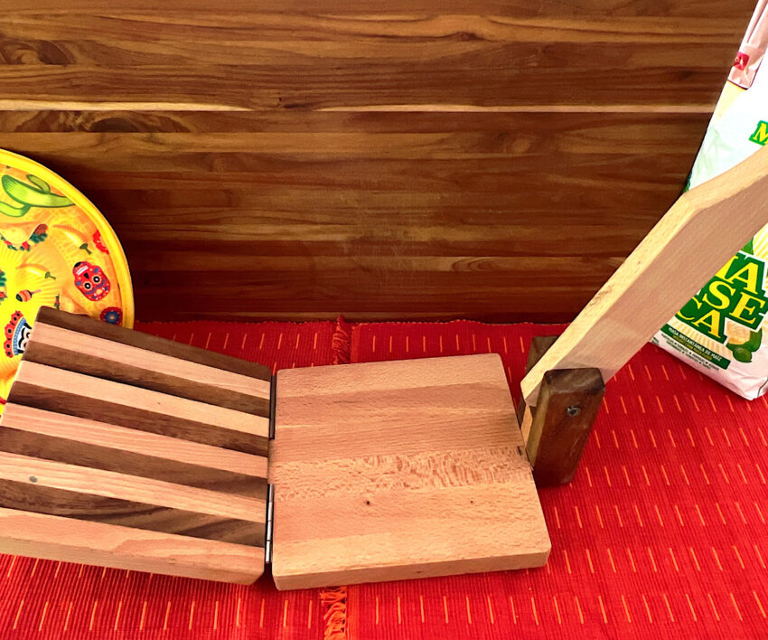 Wooden tortilla press on red tablecloth.