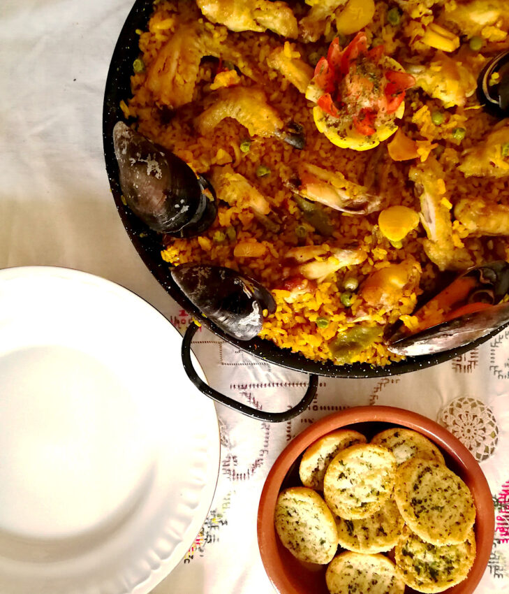 Paella “mixta” (mixed meat and seafood) in a paella pan on a table with a side of crackers.