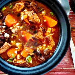 Turkey, carrot and black bean chili with mole sauce in a black bowl.