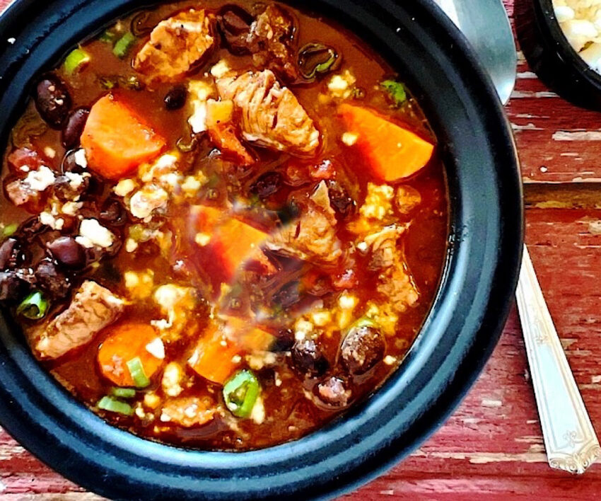 Turkey, carrot and black bean chili with mole sauce in a black bowl.