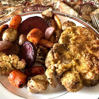 A plate filled with roasted root vegetables (carrots, beets and cauliflower) with a pork chop.
