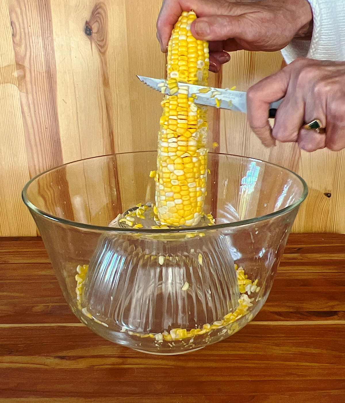 Cutting the kernels off of fresh sweet corn with a knife into a bowl.