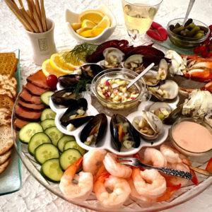 Seafood platter for 6 people with cold seafood, including shrimp, cucumber, salmon, crawfish, crab legs, cocktail sauce, mignonette sauce, crackers, wine and baby pickles.
