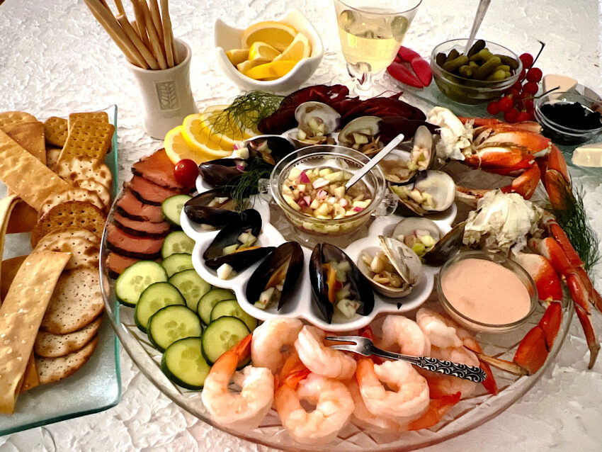 Seafood platter with shrimp, cucumber, salmon, crawfish, crab legs, cocktail sauce, mignonette sauce, crackers, wine and baby pickles.