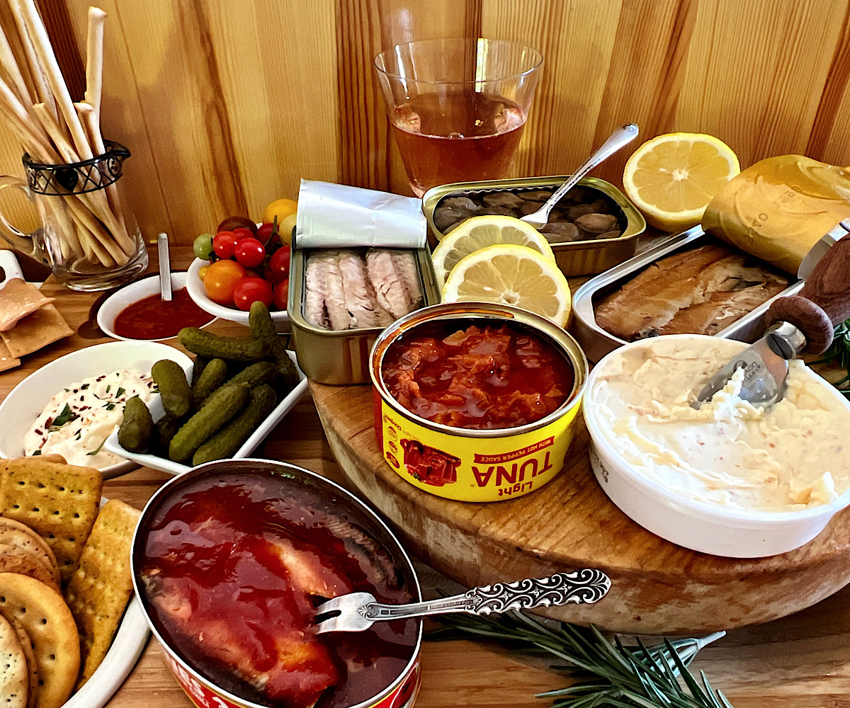 Tinned seafood platter with open tins of fish, lemons dips and crackers.