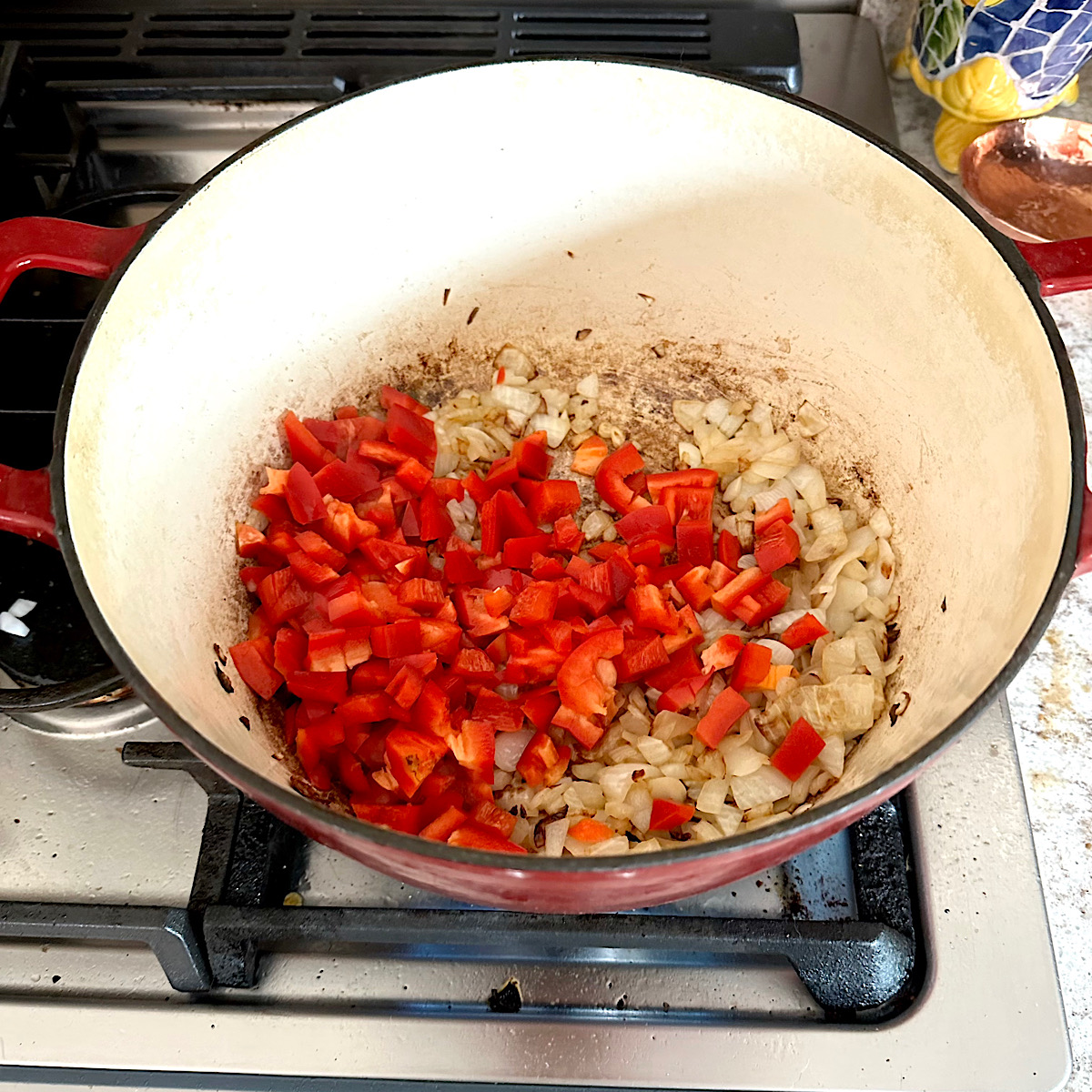 Red bell peppers cooking with the onions in a dutch oven