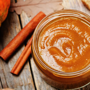 Jar of pumpkin butter with cinnamon sticks on the side.