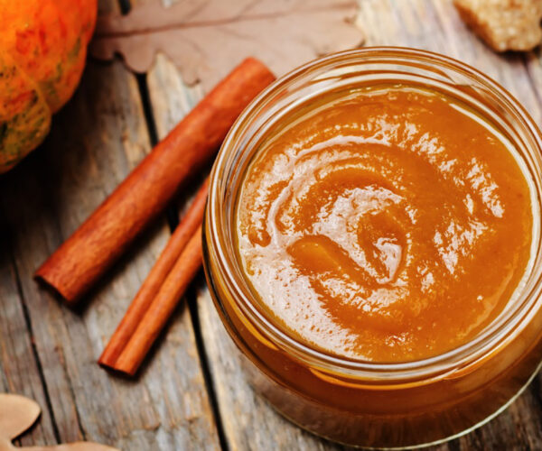 Jar of pumpkin butter with cinnamon sticks on the side.