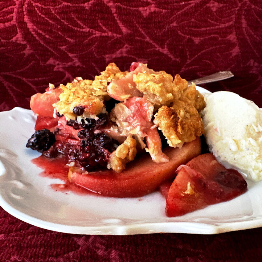 Piece of apple blackberry crumble on a white plate and maroon background.