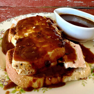Open faced turkey sandwich with red eye gravy on top and a white pitcher of gravy on the side.