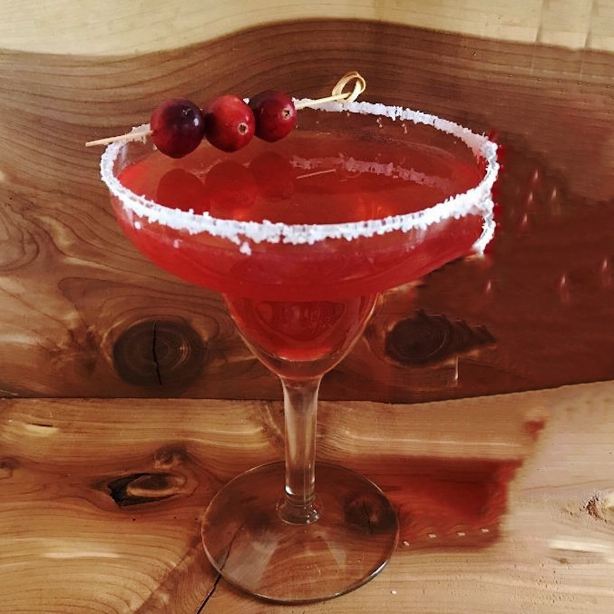 Spicy cranberry margarita with salted rim and 3 cranberries as a garnish.