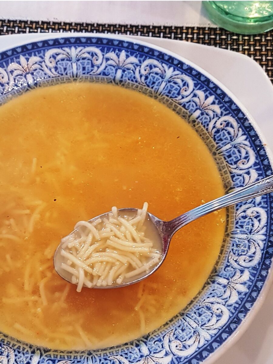 Sopa de Fideo (tomato noodle soup) in a blue bowl with a spoonful of fideo noodles.