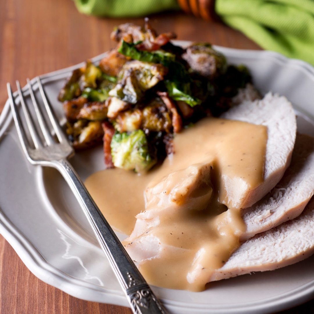 Plate of vegetables and turkey slices with turkey gravy.