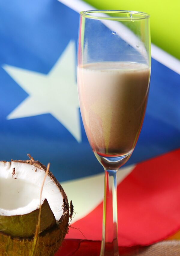 Glass of coconut eggnog with coconut on side - a Puerto Rican eggnog.