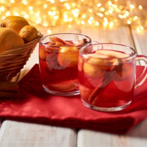 2 cups of Mexican ponche drink on red towel with lights in background.