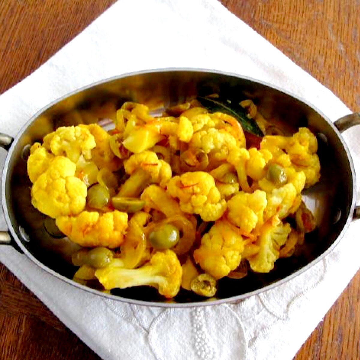 Baked cauliflower with saffron and olives in copper baking dish.