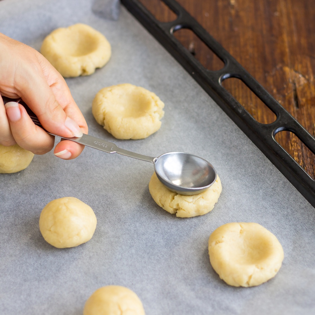 Using a spoon to make an indentation in thumbprint cookies before baking.