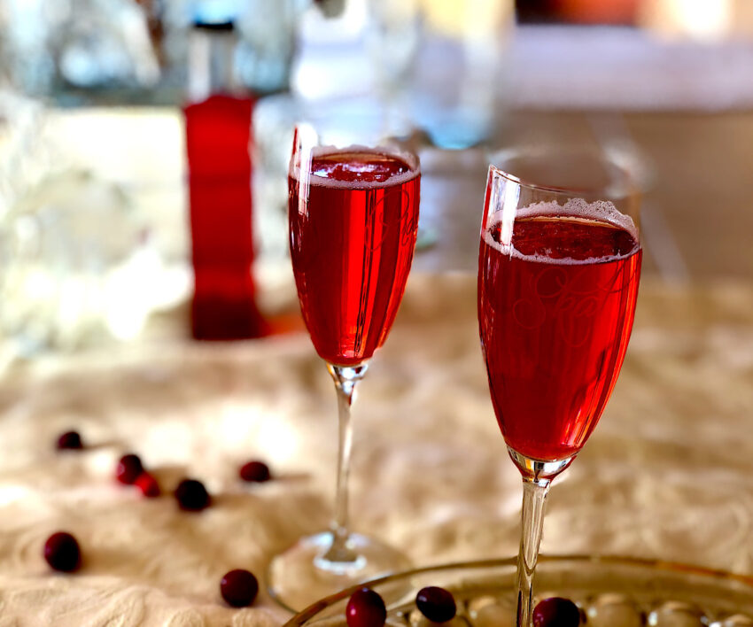 Two champagne cocktails made with a cranbery simple syrup which is in background.