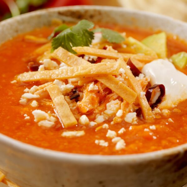 Sopa de fideo with added tortilla chips on top garnished with sour cream and cilantro.