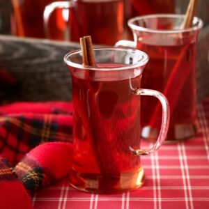 Crockpot holiday cranberry apple tea in 2 cups with a cinnamon stir stick.