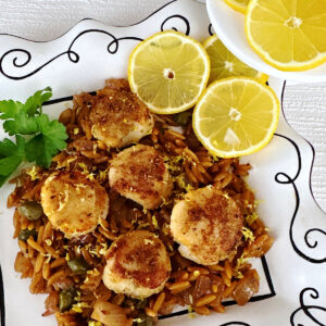 Pan seared scallops on a bed of orzo pasta garnished with lemon slices.