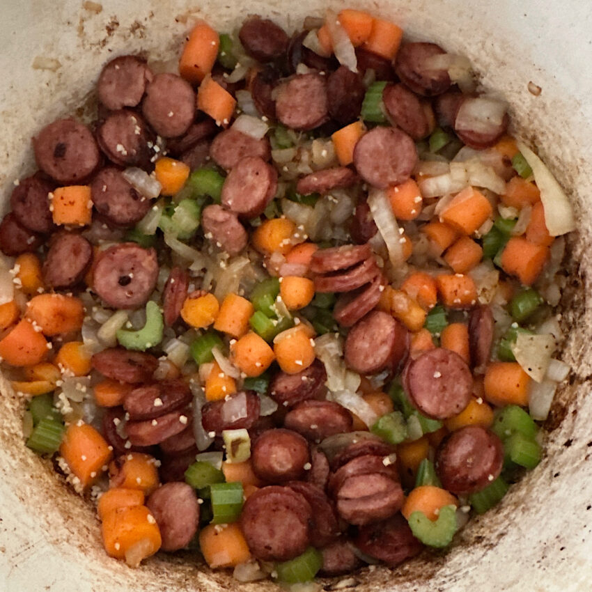 Large pot of cooked carrots, onions, celery and andouille sausage.