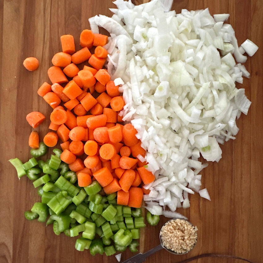 Chopped onions, carrots, celery and garlic on a cutting board.