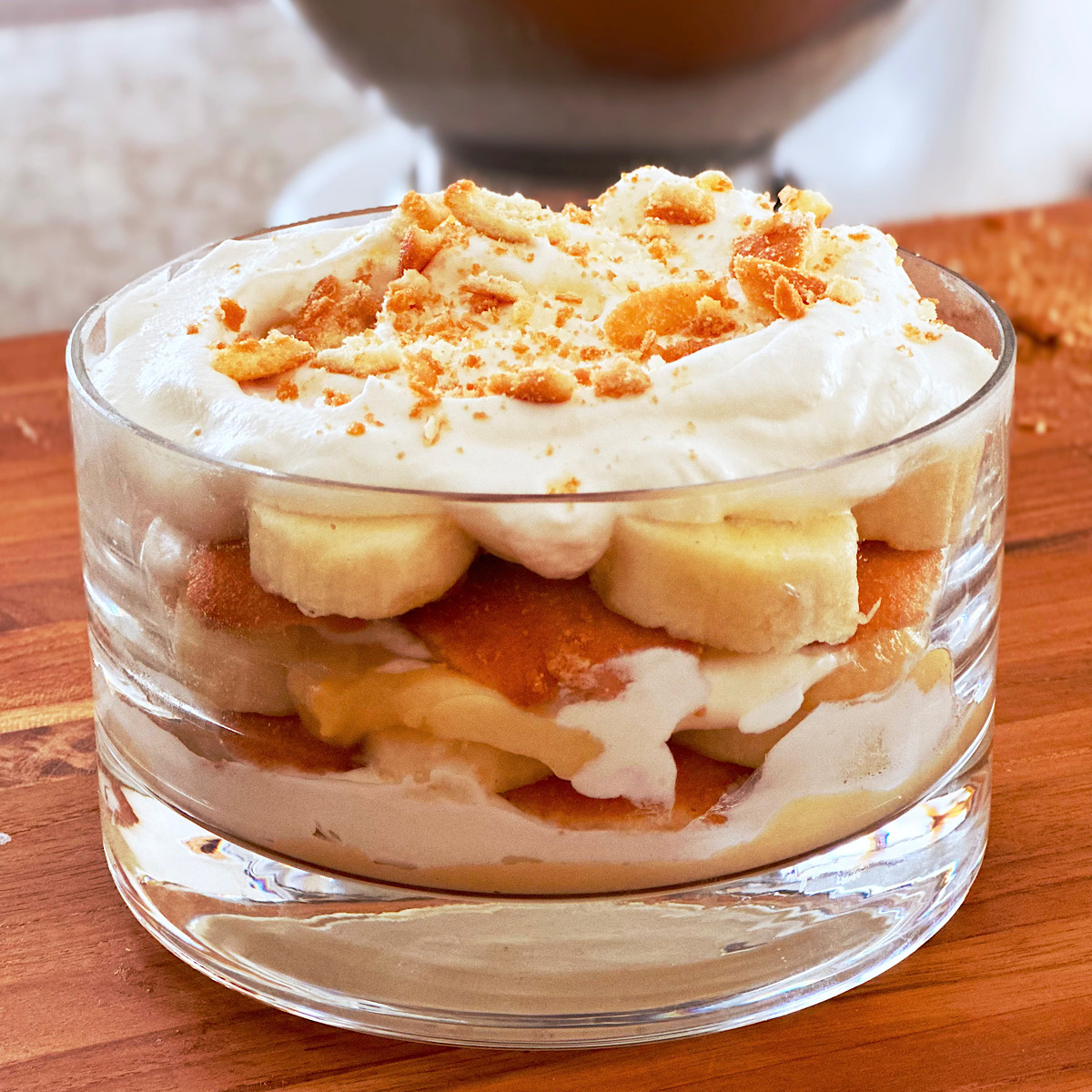 Banana Vanilla Wafer Pudding layered in glass bowl with whipped cream and wafer crumbs on top.