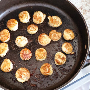 16 scallops cooking in hot oil in a skillet.
