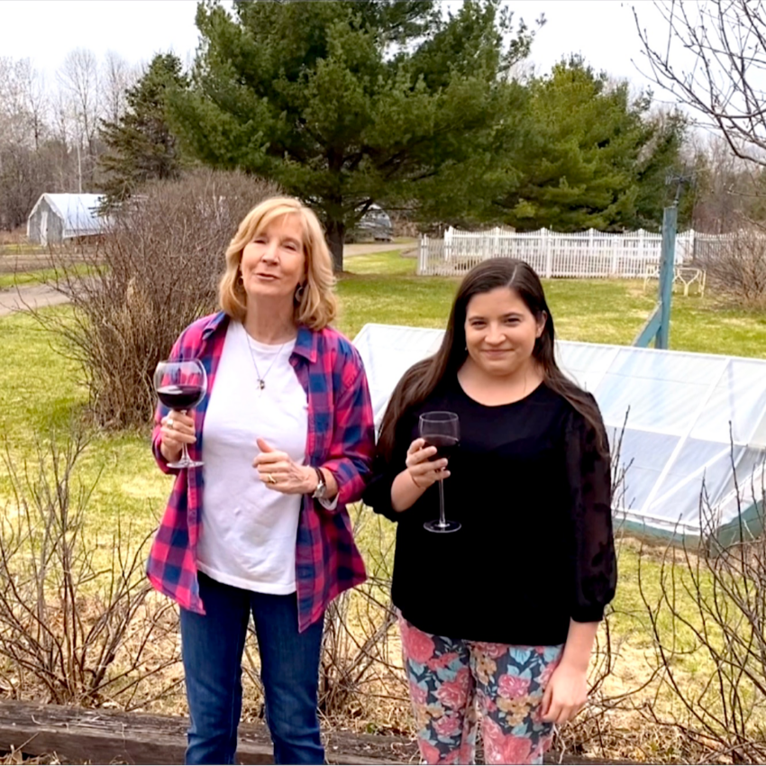 Co-owners of Heathglen Farm (Dorothy and Tesla) with a glass of wine in front of cold frame.