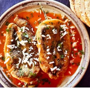 Two egg-battered chile rellenos in red sauce on a plate.