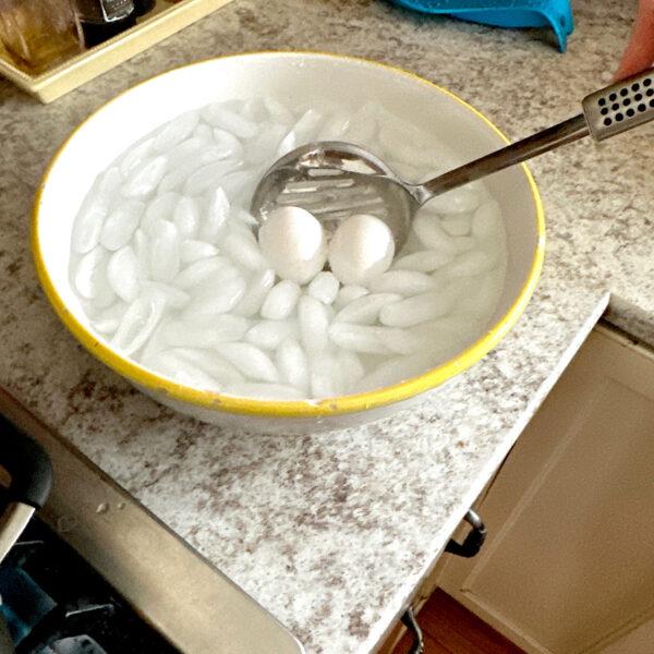 Bowl of ice water with boiled eggs being lowered in it to chill.