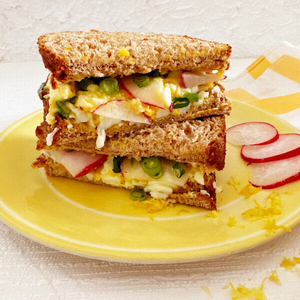 Two halves of egg salad sandwich stacked on top of each other on a yellow plate.