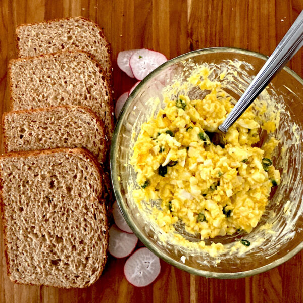 Creamy egg salad in a bowl with 4 bread slices on the side.