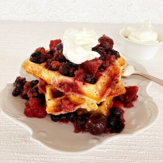 Waffles with rumtopf berry topping and whipped cream garnish