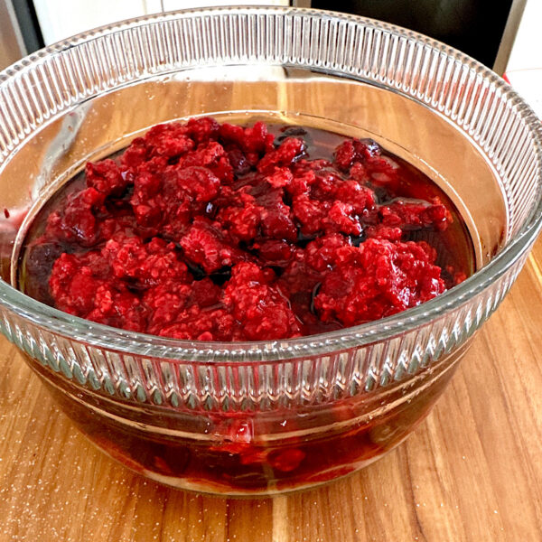 Raspberries in a glass bowl macerating in sugar.