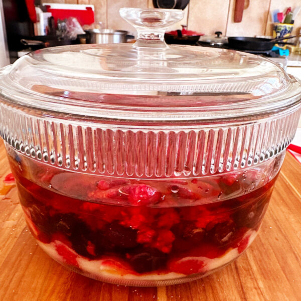 Berries in sugar and rum in a covered glass bowl ready to store for making rumtopf.