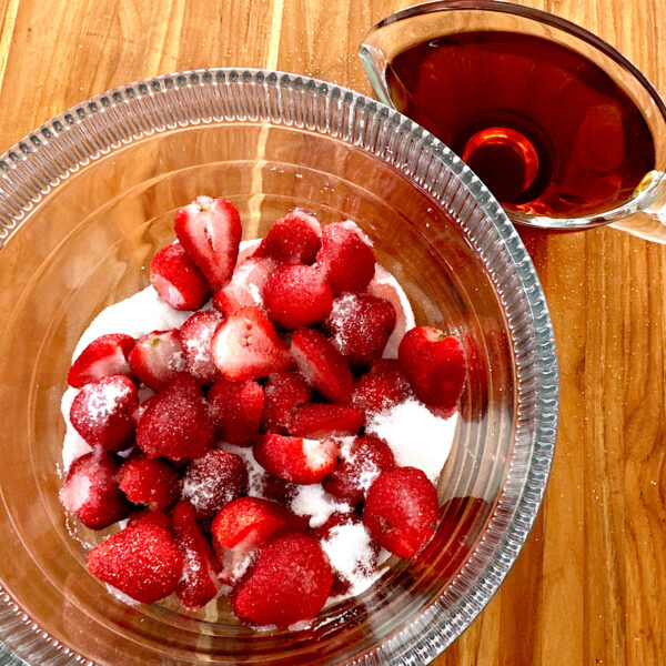 Strawberries in a glass bowl covered with sugar and a pitcher of rum on the side.