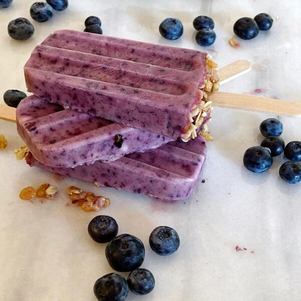 Blueberry lime and yogurt popsicles stacked on top of each other with blueberries sprinkled around.