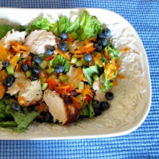 Dinner salad with chicken, greens and blueberries in a white bowl.