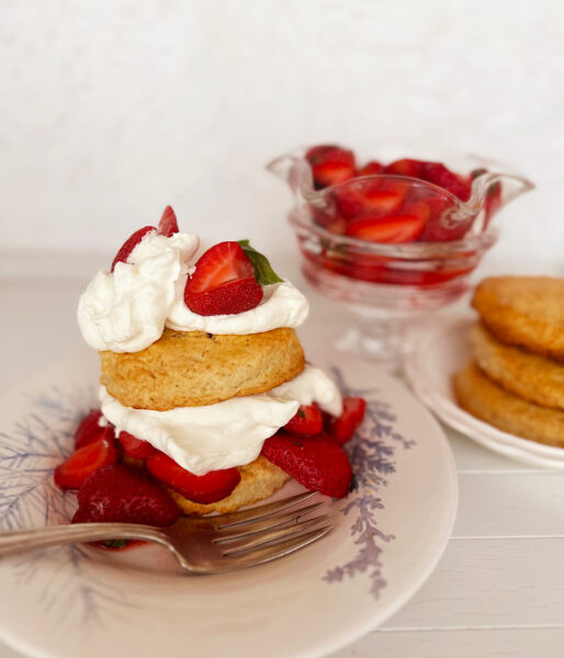 Strawberry shortcake with biscuits and strawberries in background.