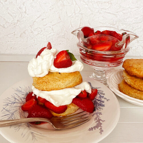Strawberry shortcake on a white plate with sides of strawberries and biscuits.
