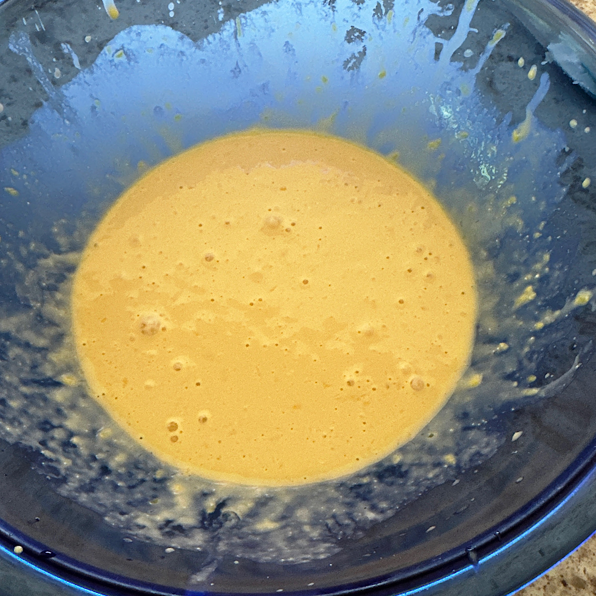 Wet ingredients (eggs, vanilla, sour cream and lemon juice) mixed together in a blue bowl.